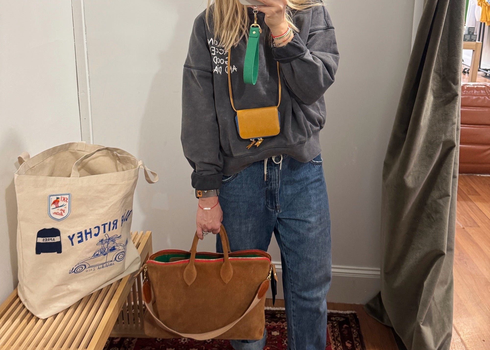 Blair Ritchey wearing a gray sweatshirt, blue jeans, and a beanie, holding a the brown suede Mini Hugh Crossbody bag.